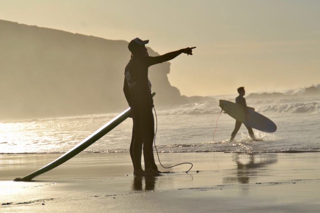 Surfer am Strand. Ein Surflehrer zeigt zeigt auf die wellen