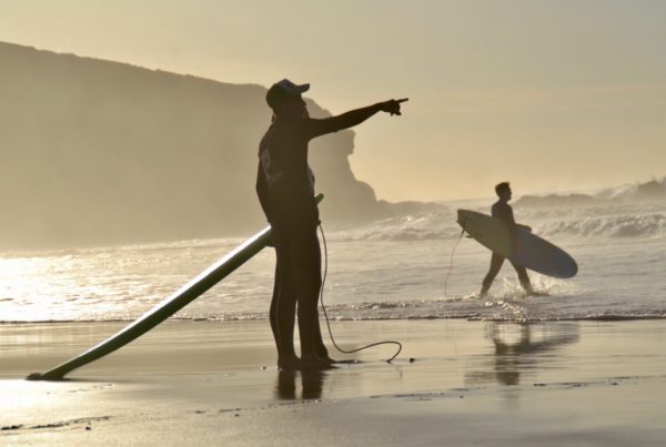 Surferi na pláži. Inštruktor surfovania ukazuje na vlny