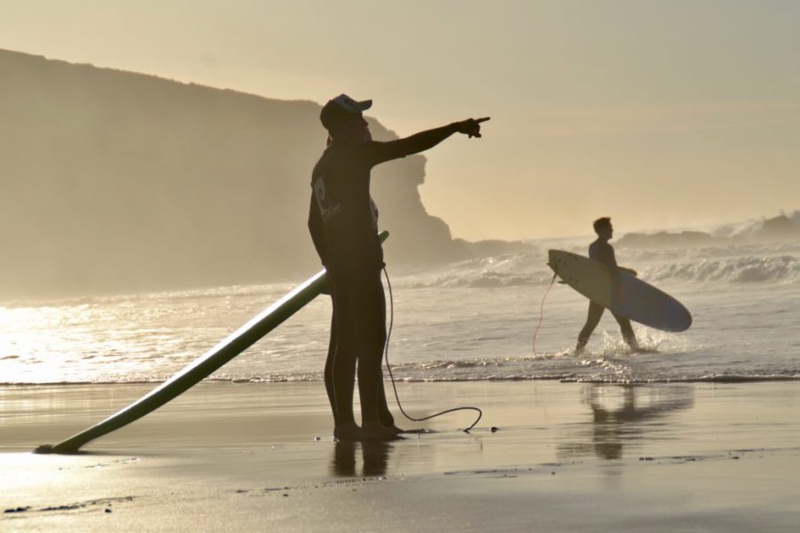 Surfer am Strand. Ein Surflehrer zeigt zeigt auf die wellen
