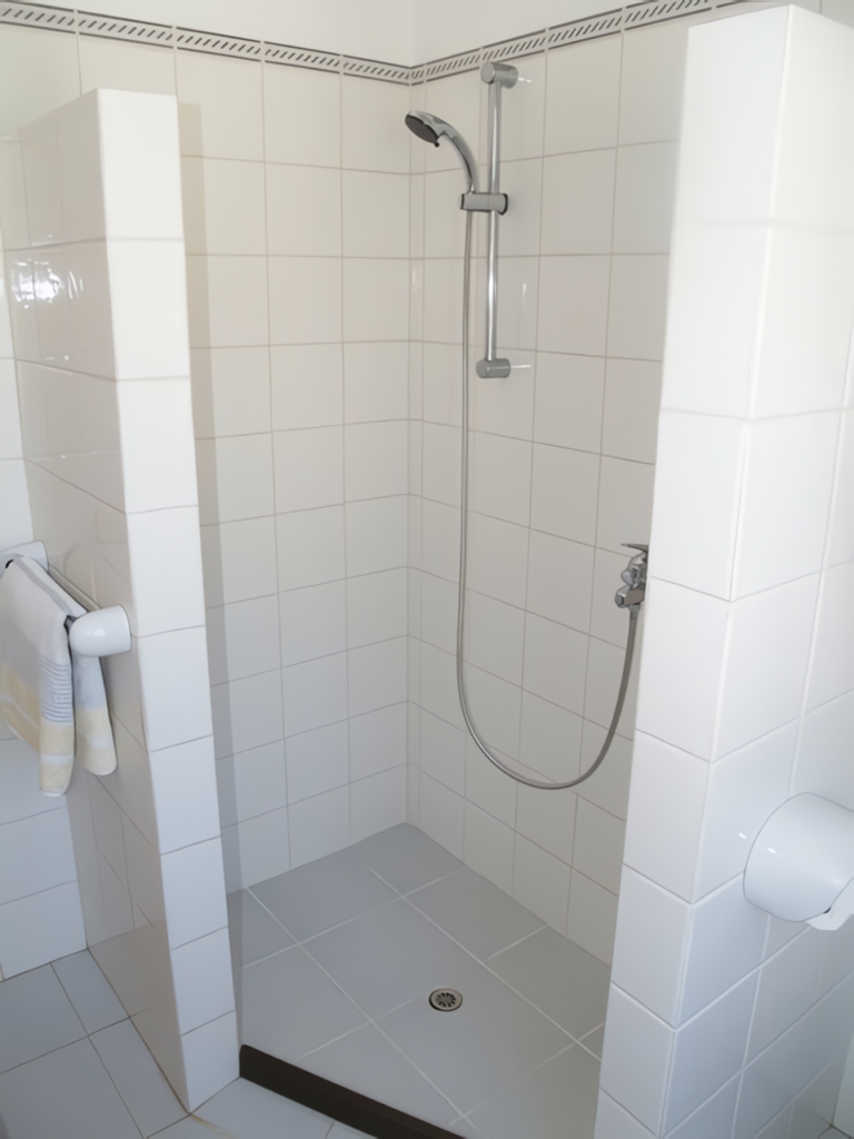 Duschbereich mit weißen Fliesen und einer Handbrause an der Wand.