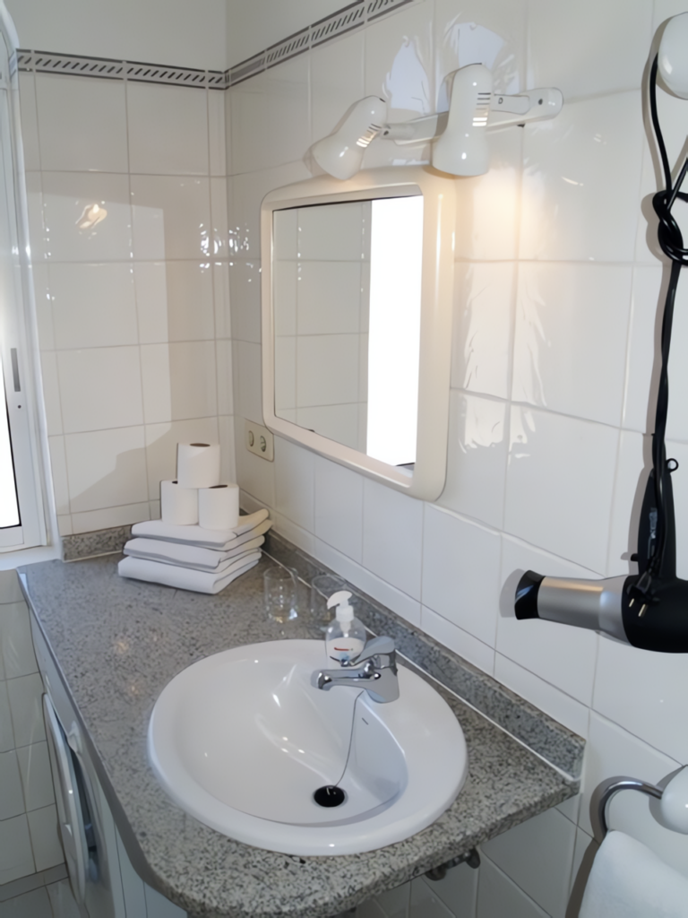 Ein Badezimmer mit einem runden Waschbecken, einem Spiegel und Handtüchern auf einer Ablage.
