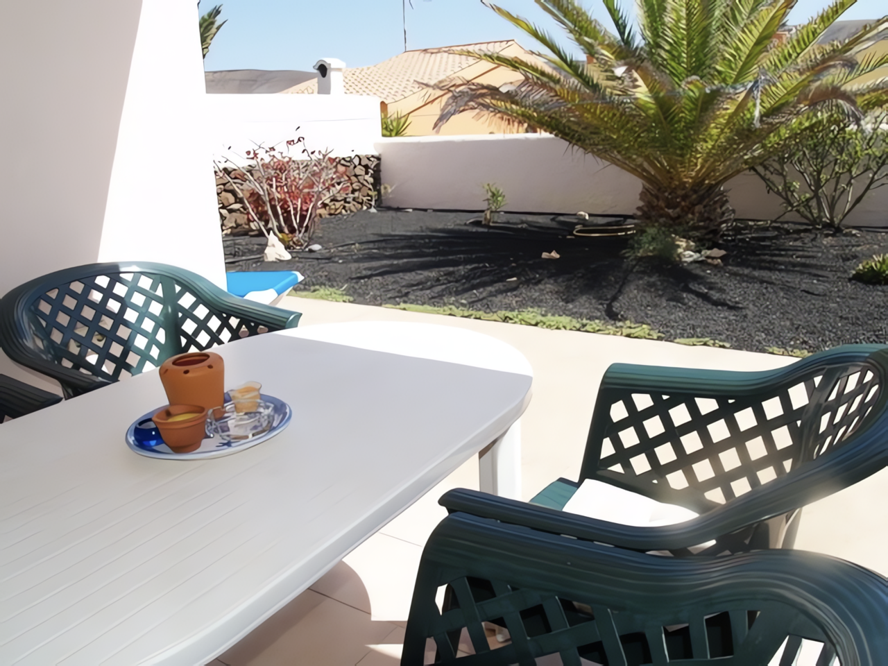 Ein Tisch mit Stühlen auf einer Terrasse, umgeben von Pflanzen und einem klaren Himmel.