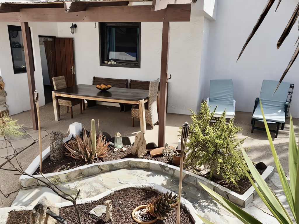 Ein Gartenbereich mit einem Holztisch, Stühlen und verschiedenen Pflanzen in Töpfen.
