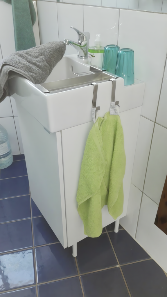Weißes Waschbecken mit grauem Handtuch, grünen Gläsern und einem grünen Handtuch im Badezimmer.