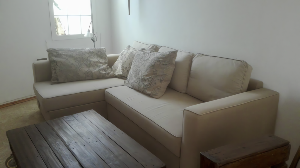 Beige Sofa mit dekorativen Kissen und einem rustikalen Holztisch im Vordergrund.