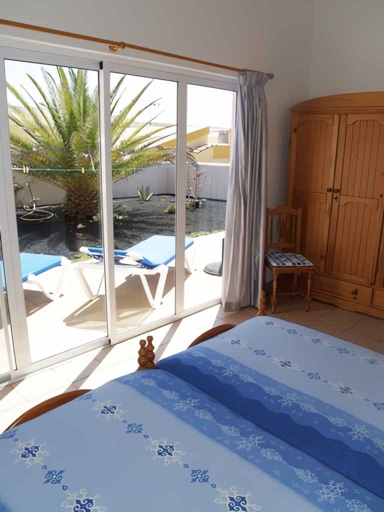 Ein Schlafzimmer mit einem Bett und einem Holzschrank, Blick auf eine Terrasse mit Pflanzen.
