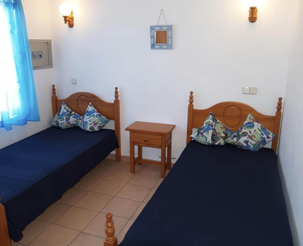 Schlafzimmer mit zwei Einzelbetten, blauen Bettlaken und dekorativen Kissen auf einem Nachttisch.