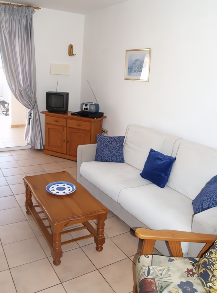 Ein Wohnzimmer mit einem weißen Sofa, einem Couchtisch und einem Fernseher auf einem Sideboard.