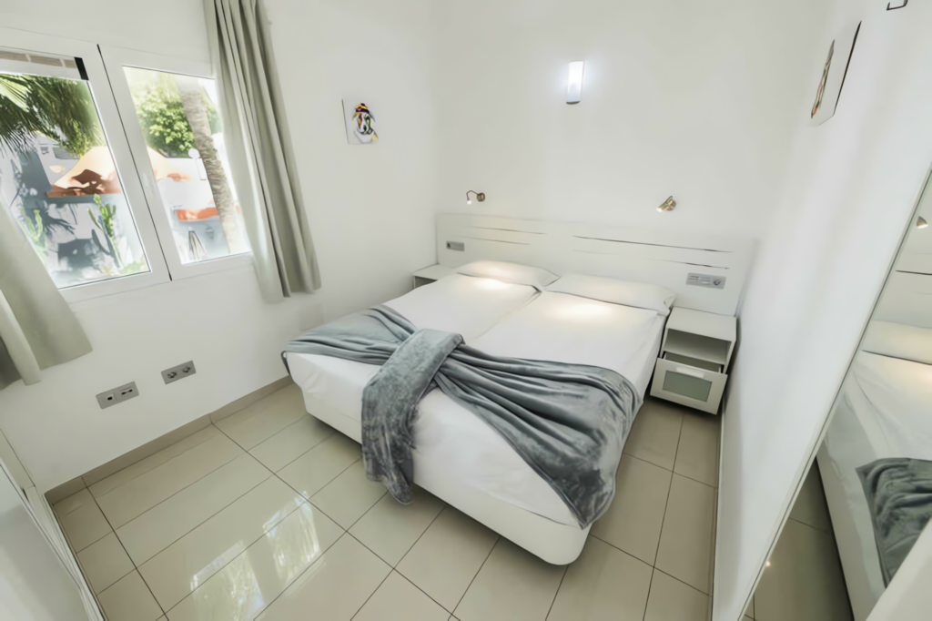 Helles Schlafzimmer mit einem Doppelbett, einem grauen Überwurf und einem großen Spiegel an der Wand.