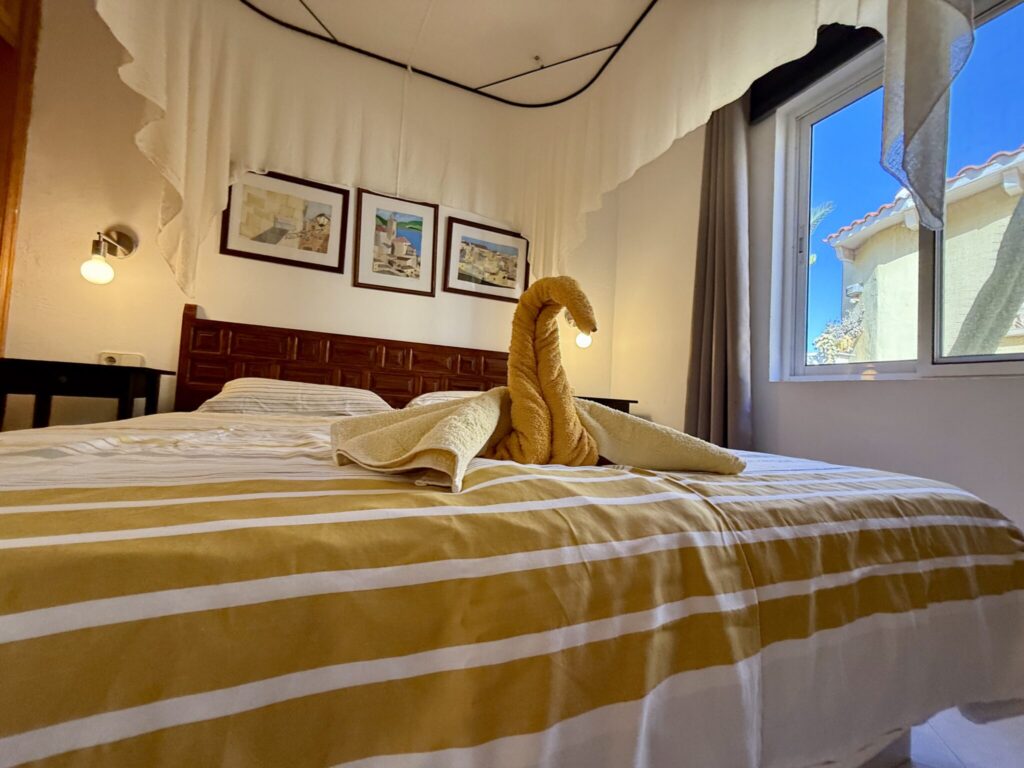 Ein Bett mit gelben Handtüchern, darunter ein gefaltetes Handtuch in Form eines Schwans, und Wandbildern im Hintergrund.