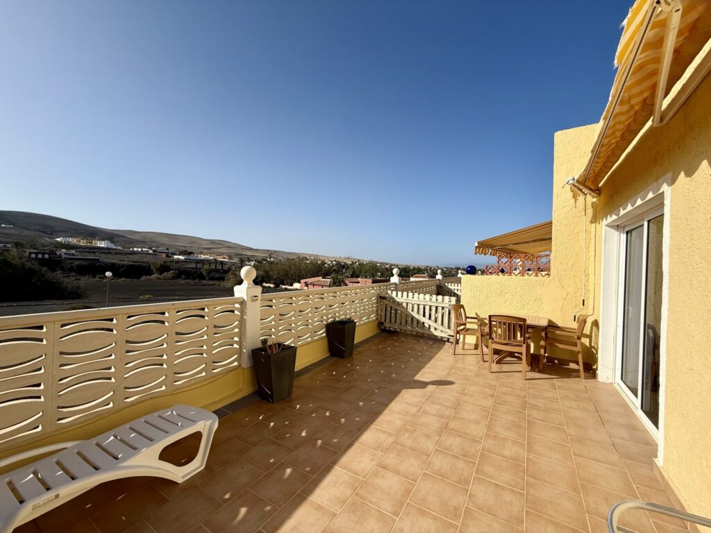 Balkon mit Aussicht auf Fuerteventura Balkon mit gelber Wand und Terrakotta-Fliesen, ausgestattet mit Liegestuhl und Tisch.