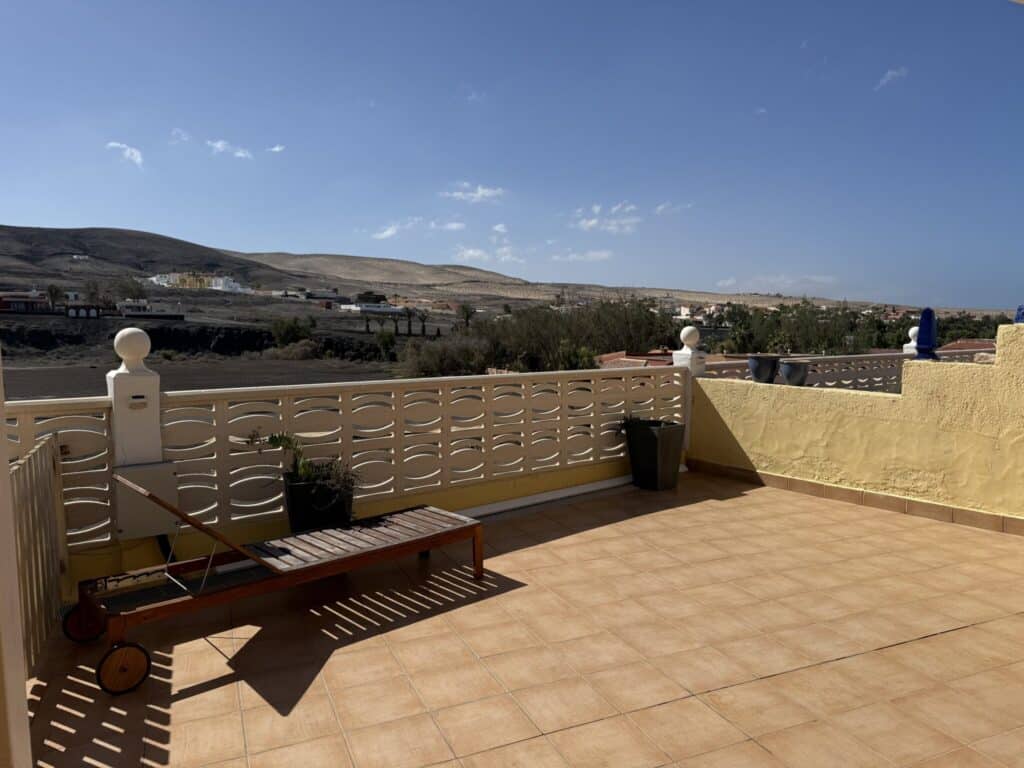 Terrasse mit einer Liege und Blick auf eine hügelige Landschaft unter blauem Himmel.