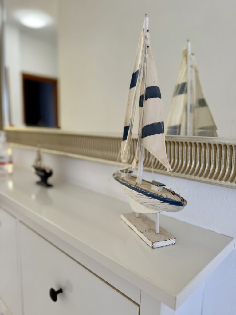 Modellboot mit Segeln auf einem Tisch Ein Modellboot mit weißen und blauen Segeln steht auf einem Tisch vor einem Spiegel.