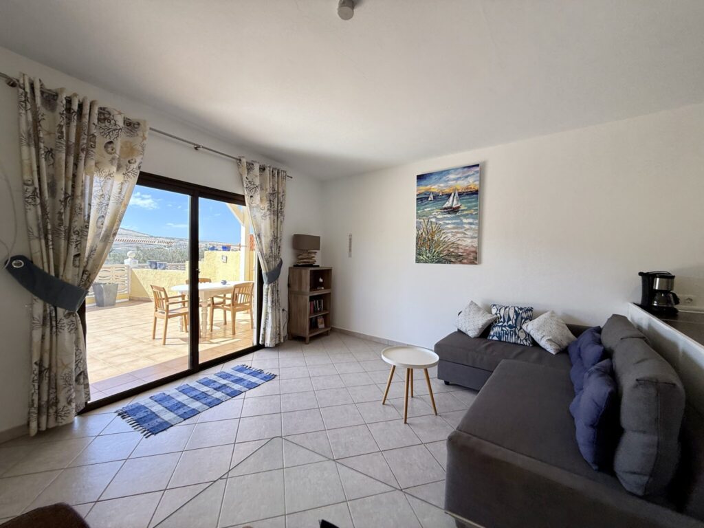 Wohnzimmer mit Sofa und Aussicht auf die Terrasse Wohnzimmer mit grauem Sofa, Tisch und Zugang zur Terrasse mit Blick auf die Landschaft.