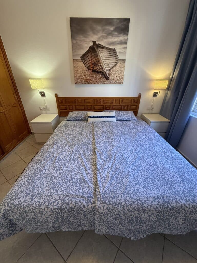 Doppelbett mit blauer Bettwäsche und einem Wandbild eines Bootes im Hintergrund.