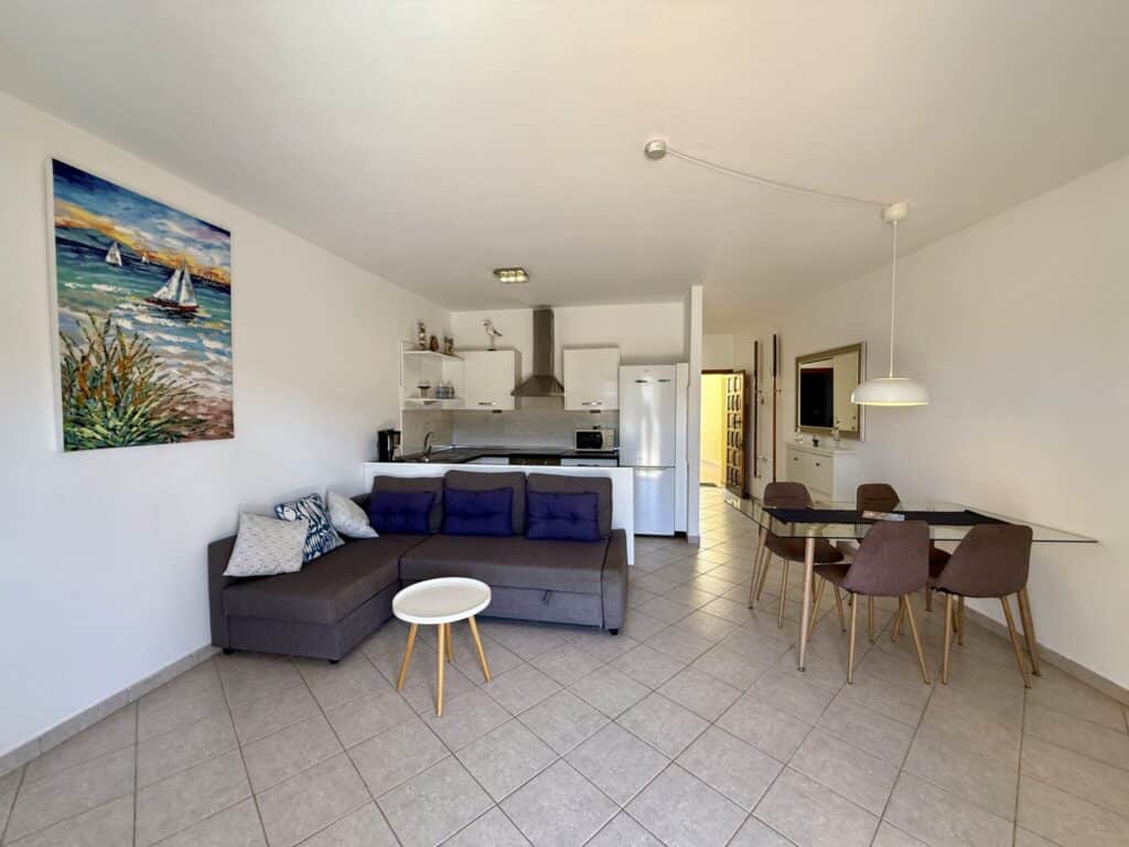 Helles Wohnzimmer mit einer Couch, einem Tisch und einer offenen Küche in einem Apartment.