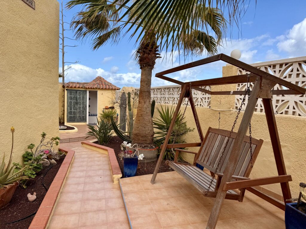 Schaukelstuhl im Innenhof eines Apartments auf Fuerteventura Holzschaukelstuhl im Innenhof eines Apartments mit Pflanzen und Palmen.