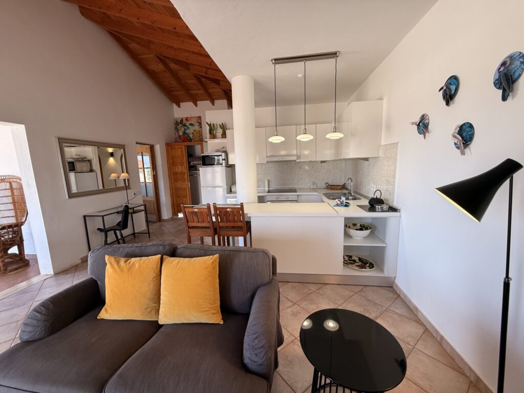 Wohnzimmer mit offener Küche in einer Ferienwohnung Wohnzimmer mit grauem Sofa, Tisch und offener Küche in einer Ferienwohnung auf Fuerteventura.