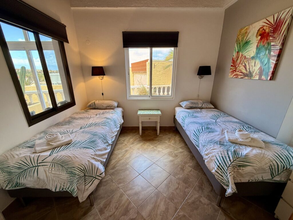 Zwei Einzelbetten in einem Zimmer mit Fenster Zwei Einzelbetten mit weißen Bettwäsche und einem kleinen Tisch in einem hellen Zimmer.