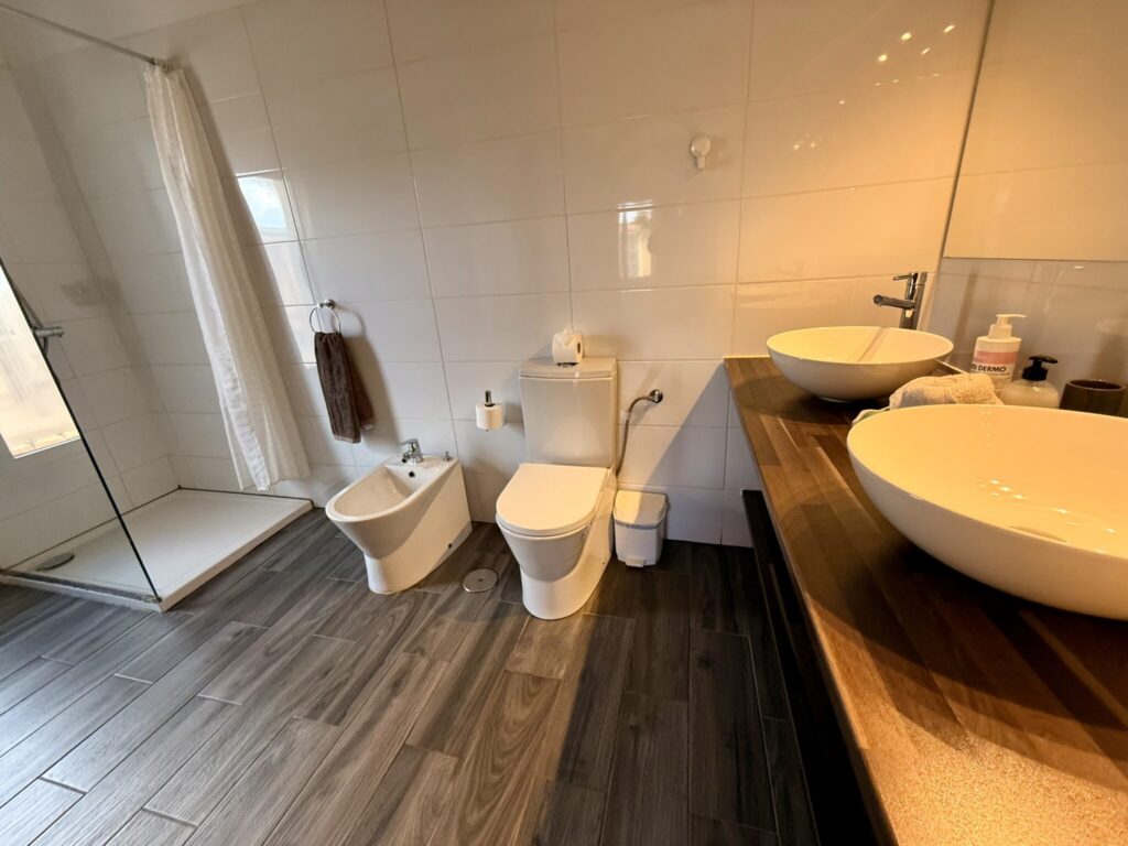 Badezimmer mit Dusche und Waschbecken Modernes Badezimmer mit Dusche, Toilette, Bidet und zwei Waschbecken auf Holzarbeitsplatte.