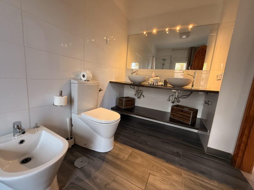 Badezimmer mit modernen Sanitäranlagen und Spiegel Helles Badezimmer mit zwei Waschbecken, Toilette und Bidet, sowie einem großen Spiegel über dem Waschbecken.