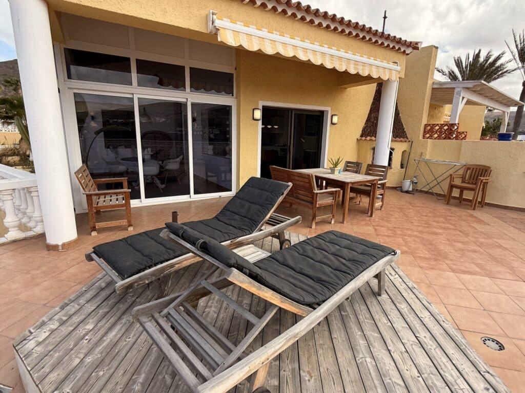 Terrasse mit Liegestühlen und Esstisch Zwei schwarze Liegestühle aus Holz auf einer Terrasse mit einem Esstisch im Hintergrund.