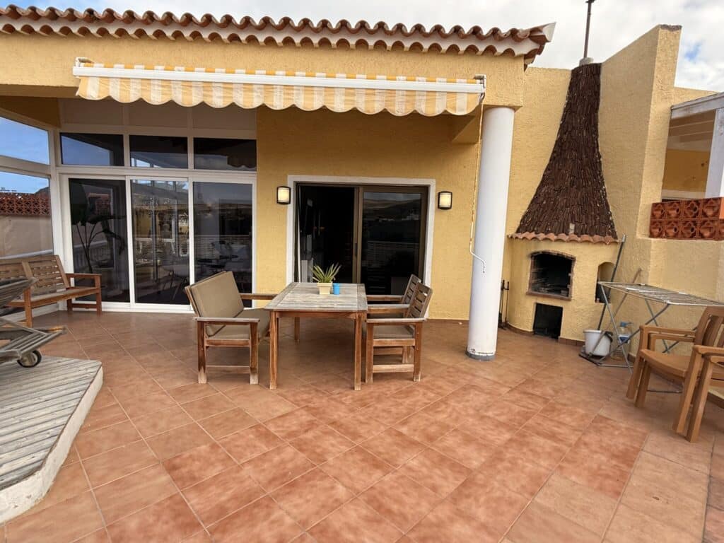 Terrasse mit Holzstühlen und Tisch Terrasse mit einem Holztisch und Stühlen, einem Sonnenschirm und einem Grill im Hintergrund.