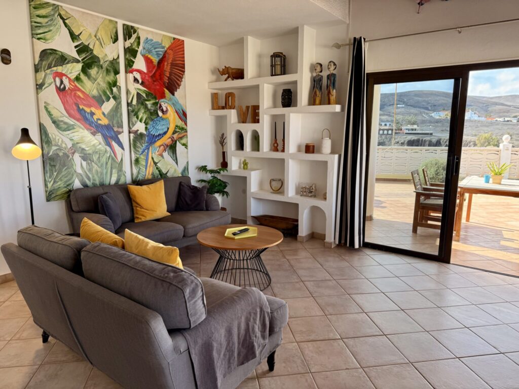 Wohnzimmer mit bunten Wandbildern und Möbeln Wohnzimmer mit zwei bunten Papageien-Wandbildern und einer grauen Couch mit Kissen.