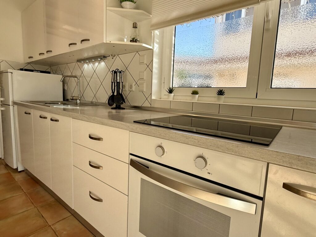 Moderne Küche mit einem Kochfeld, Kühlschrank und weißen Schränken unter einem Fenster.