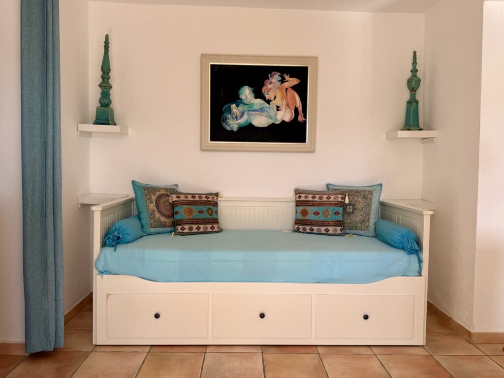 Schlafsofa mit blauer Decke und dekorativen Kissen vor einem Kunstwerk an der Wand.