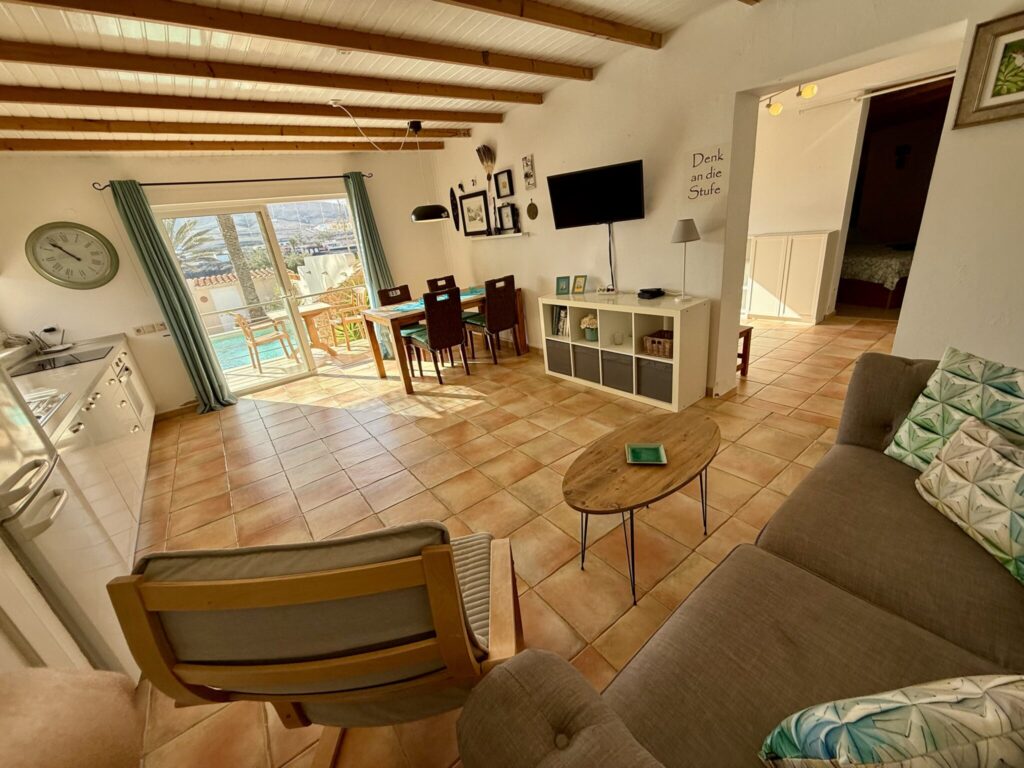 Helles Wohnzimmer mit Sofa, Tisch, Stühlen und Zugang zu einem Balkon.