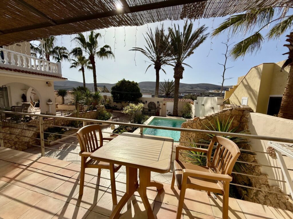 Terrasse mit Blick auf den Pool und Palmen Holztisch und Stühle auf einer Terrasse mit Blick auf einen Pool und Palmen.