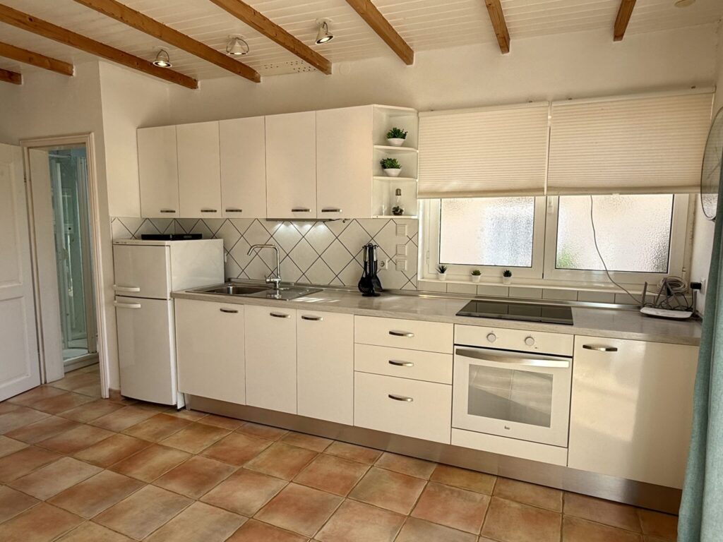 Moderne Küche mit weißen Schränken, Herd, Kühlschrank und Fenster für Tageslicht.