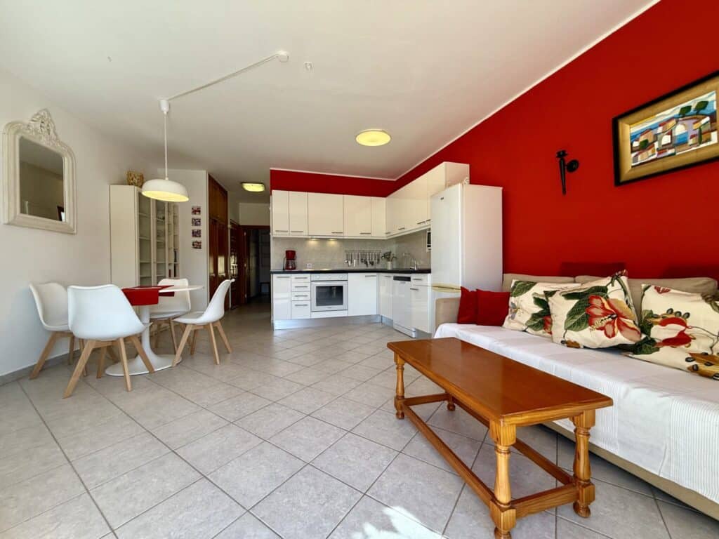 Wohnzimmer mit offener Küche, roter Wand und Möbeln in neutralen Farben.