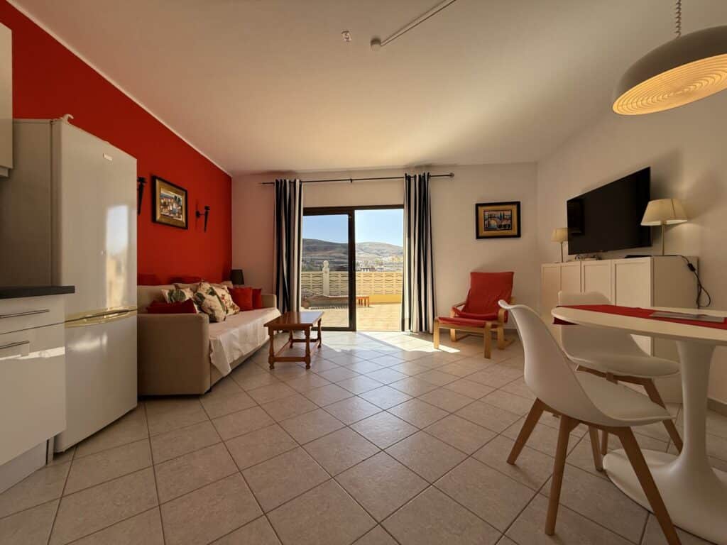 Innenansicht eines Apartments mit roter Wand, Sofa, Tisch und Stühlen in La Pared, Fuerteventura.