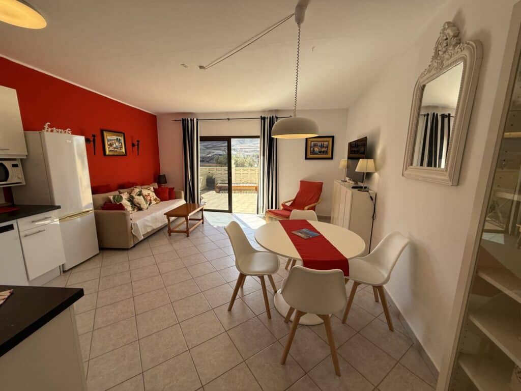 Helles Wohnzimmer mit roter Wand, Sofa, Esstisch und Stühlen im Surfcamp-Apartment.