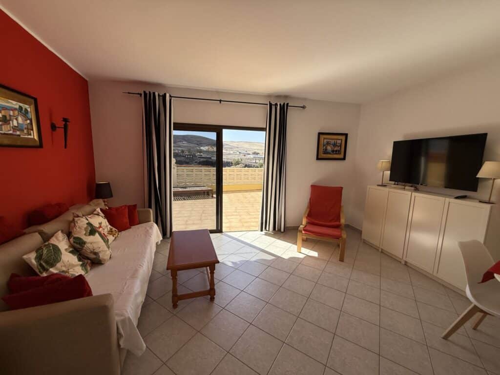 Wohnzimmer mit roter Wand, Sofa, Fernseher und Blick auf die Terrasse.