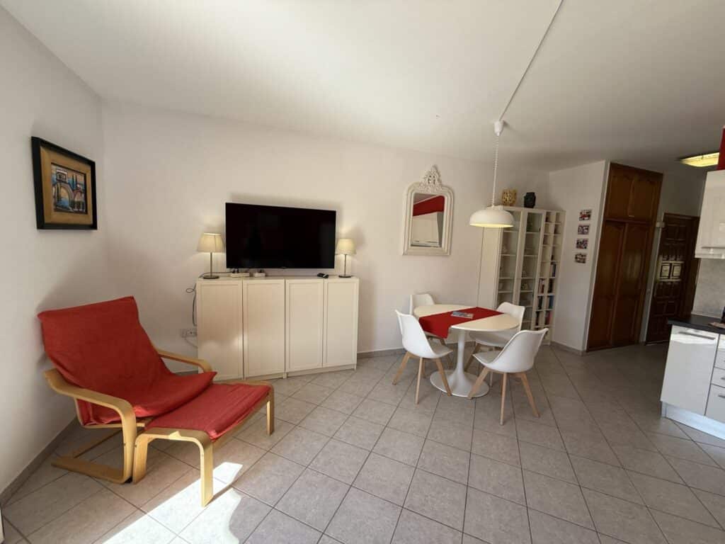 Helles Wohnzimmer mit einem Fernseher, einem Esstisch und einem roten Sessel.