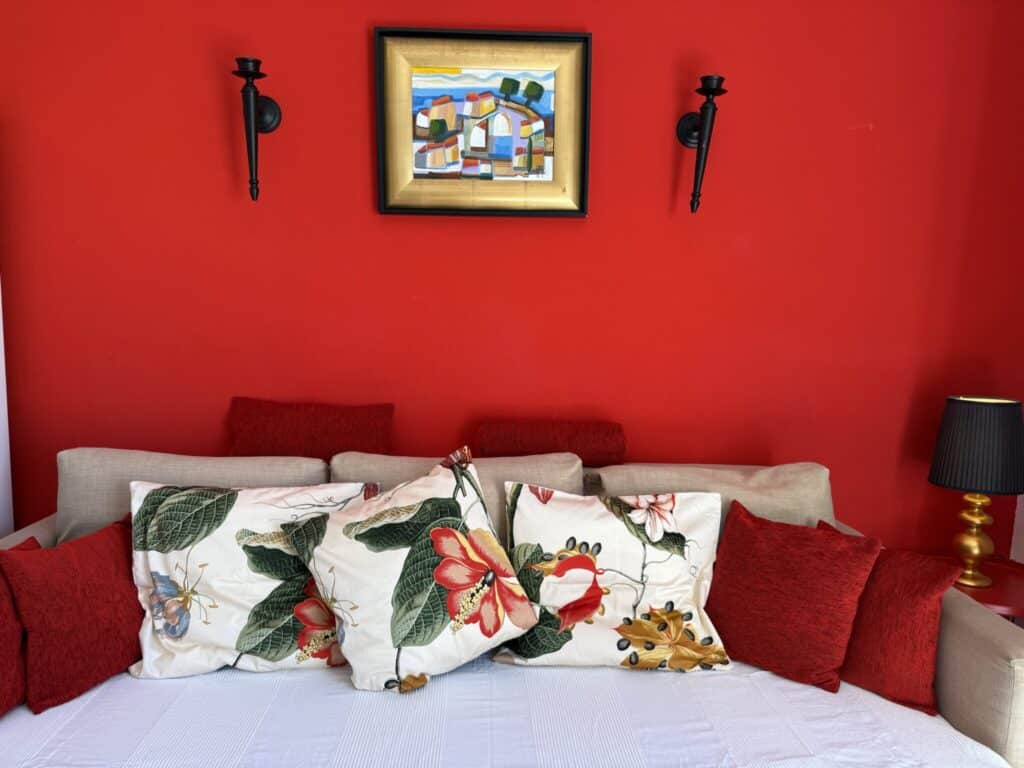 Sofa mit bunten Kissen und einem Gemälde an einer roten Wand.